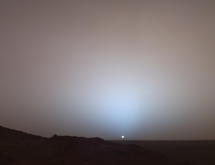sunset at mars(The white-blue sun setting over the rocky and darkened red landscape creates a surreal photograph of a truly alien landscape.