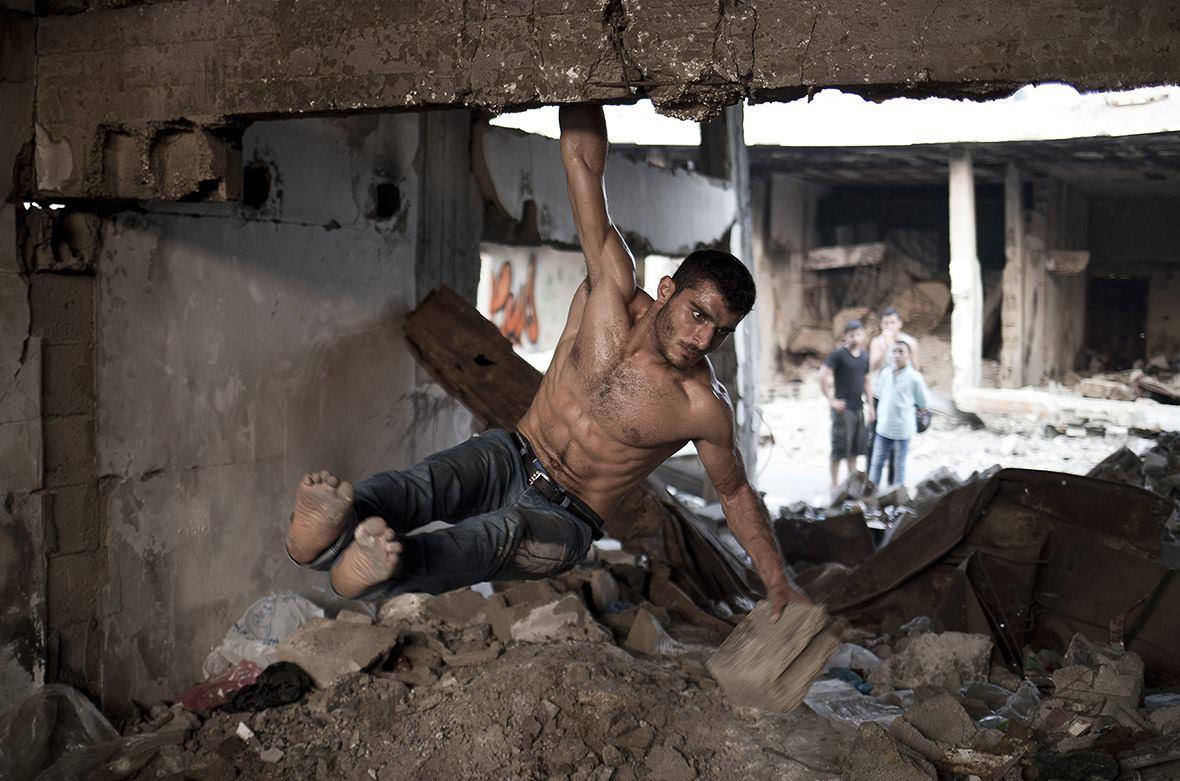 33. A man does a street workout using gravity and rubble amidst the ruins of bombed out buildings in Gaza City